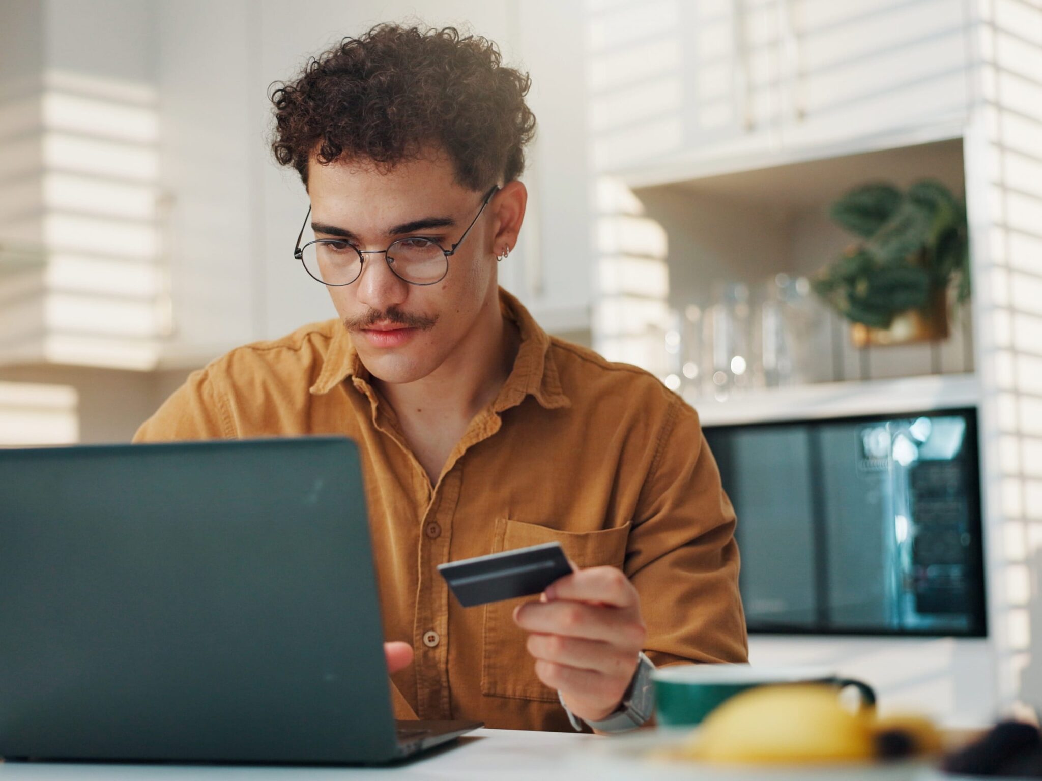 Mann mit Brille hält Kreditkarte und tippt auf Laptop für E-Commerce Checkout.